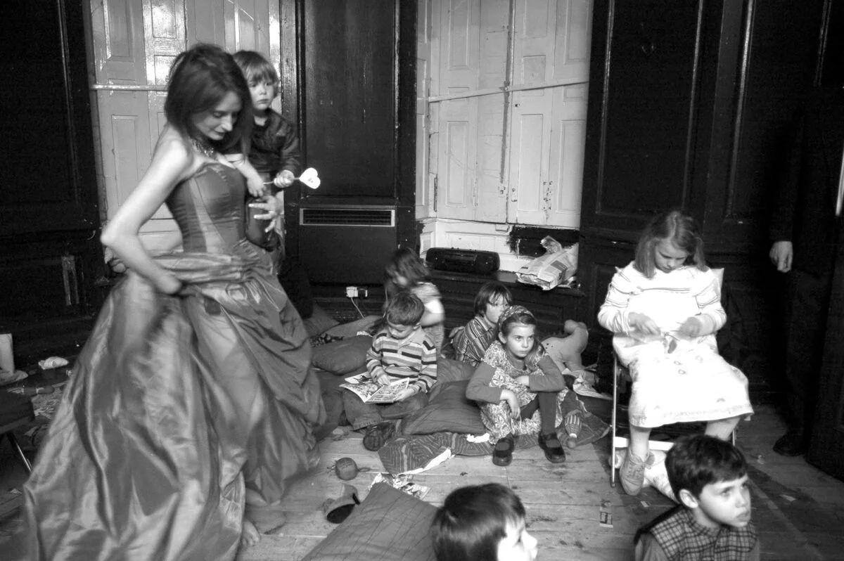 A black and white photo of a woman in a dress with children around her.