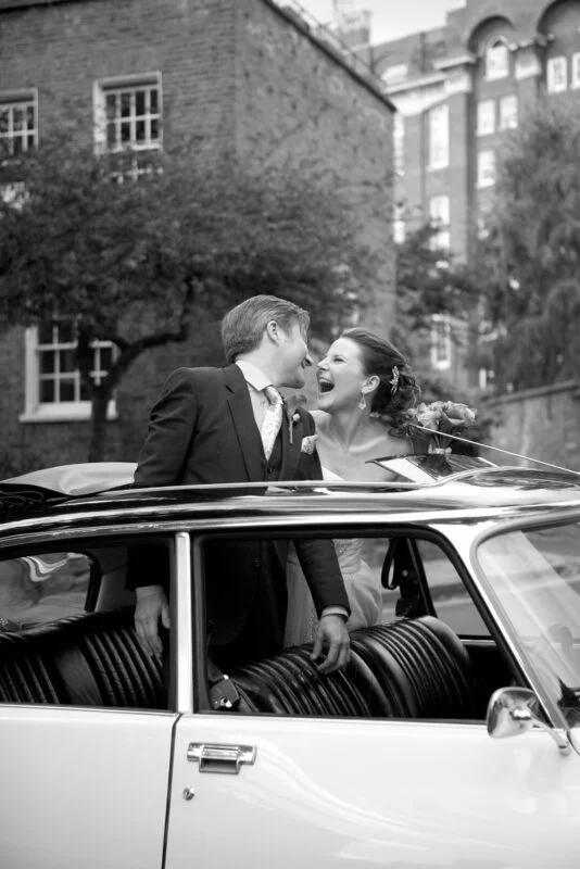 Black and white photo of a bride and groom kissing in a car.