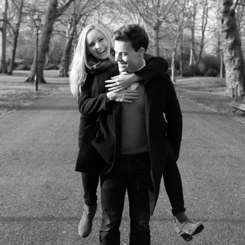 A black and white photo of a man carrying a woman in a park.