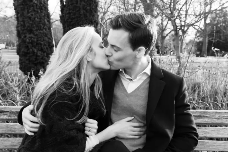 Black and white photo of a couple kissing on a park bench.