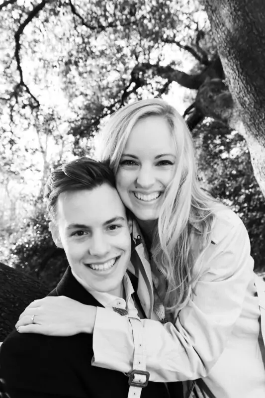 A black and white photo of a couple hugging under a tree.
