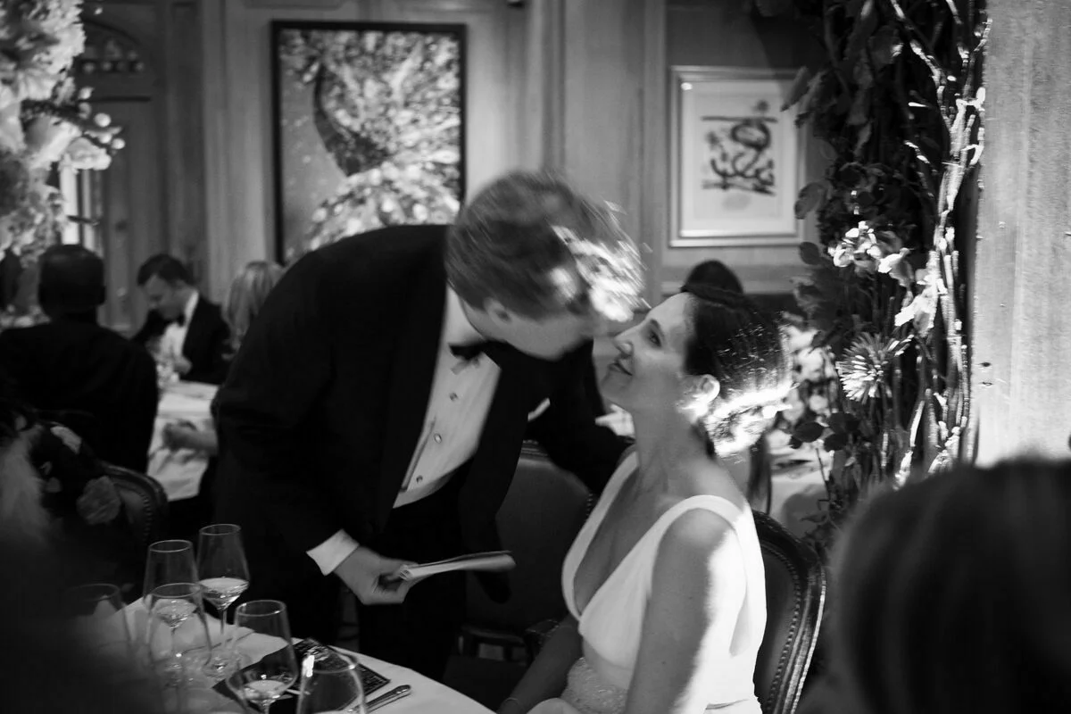 A bride and groom kissing at a dinner table.