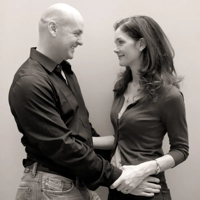 A black and white photo of a man and woman in front of a wall.