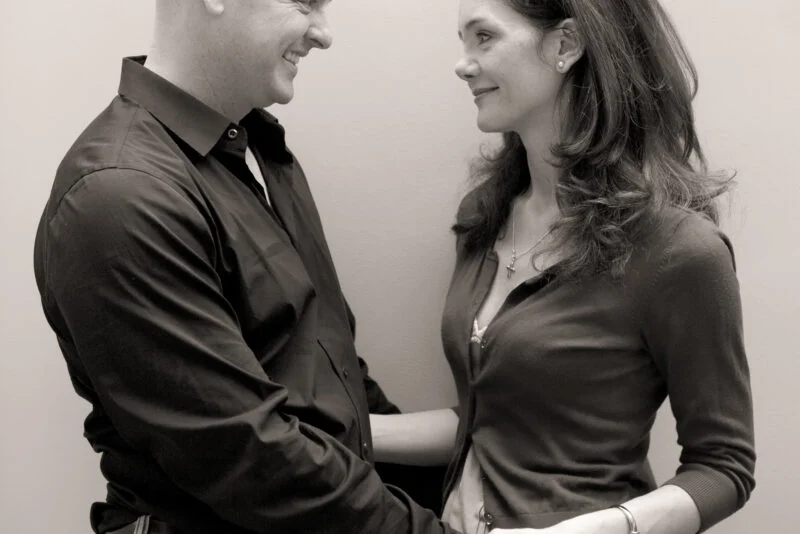 A black and white photo of a man and woman in front of a wall.