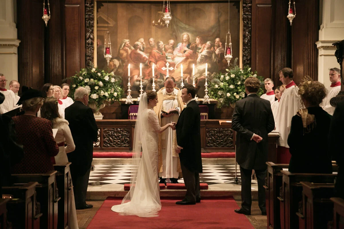 A bride and groom standing in front of a painting in a church.