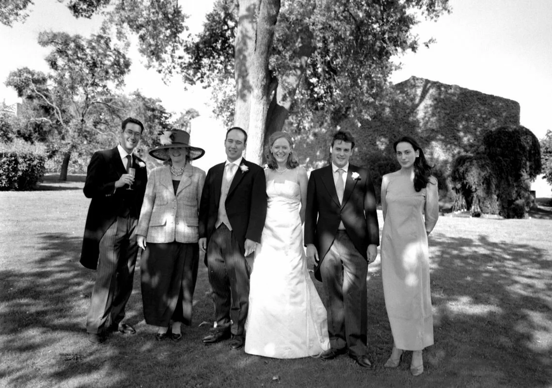A black and white photo of a wedding party posing in front of a tree.