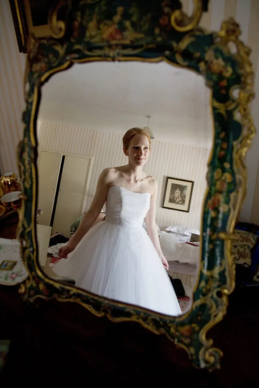 A woman in a wedding dress is standing in front of a mirror.