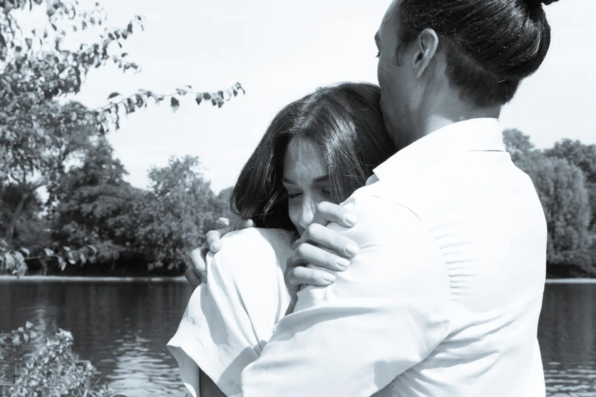 A man and woman hugging in front of a lake.