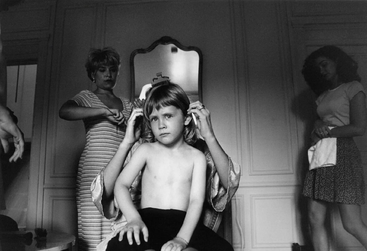 A black and white photo of a young boy getting his hair done.