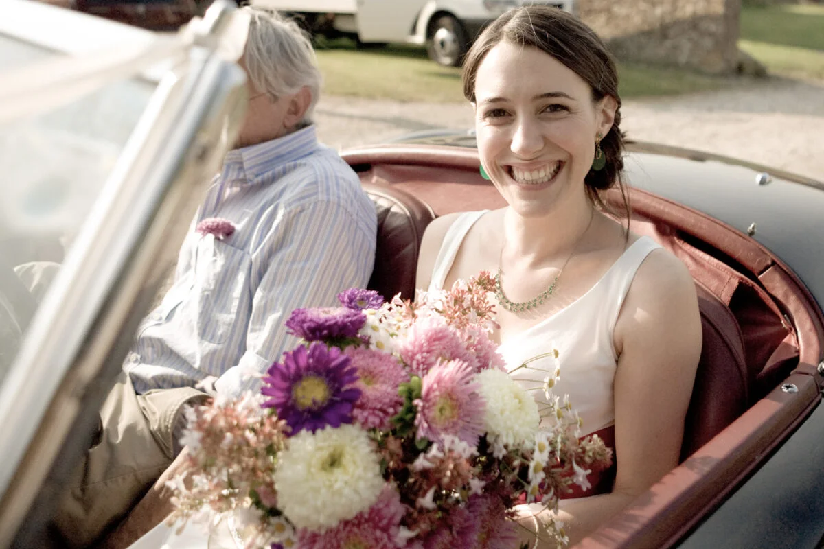 A woman sitting in a vintage car with a bouquet of flowers.