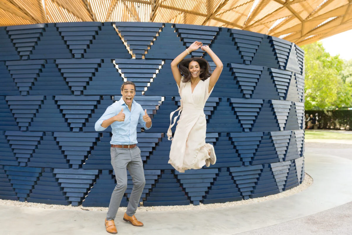 A man and woman jumping in front of a blue structure.