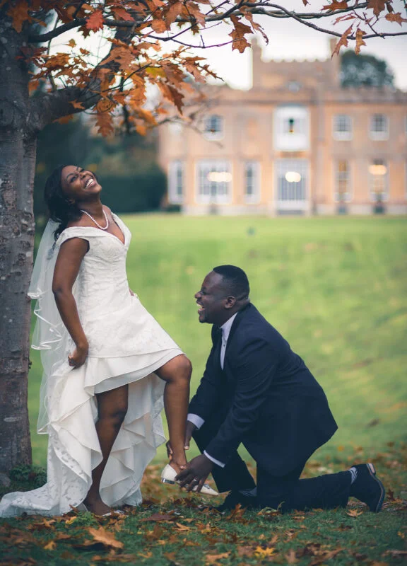 A bride and groom kneeling in front of a large mansion.