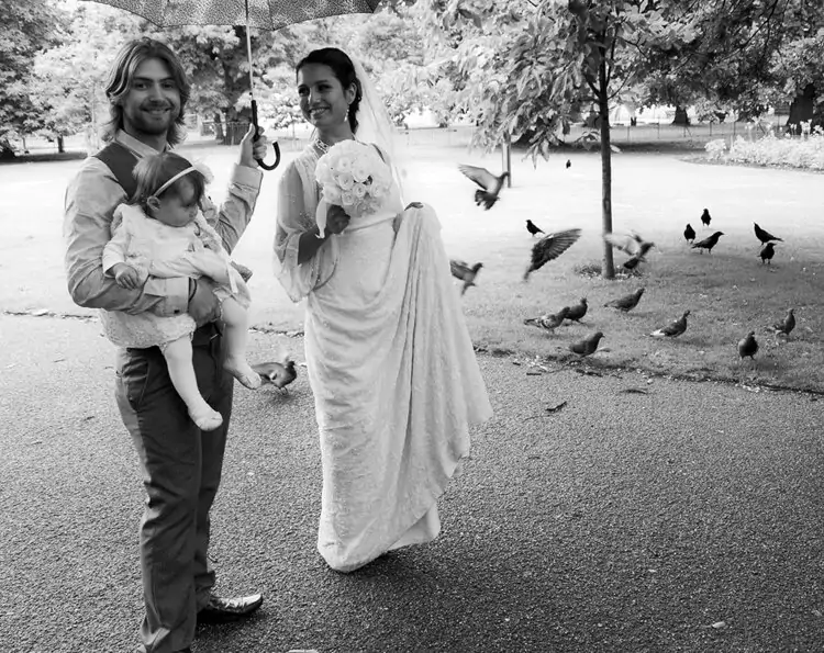 Black and white photo of a bride and groom with a baby and pigeons.