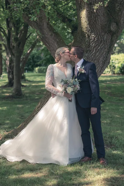 A bride and groom kissing under a tree.