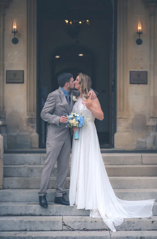 A bride and groom kiss on the steps of an old building.
