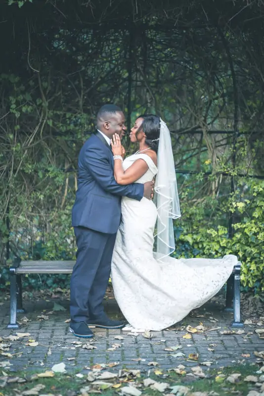 A bride and groom embracing on a bench in a garden.