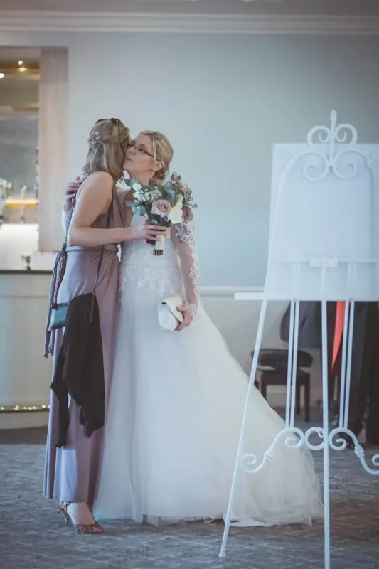A bride kisses her bridesmaid in front of an easel.