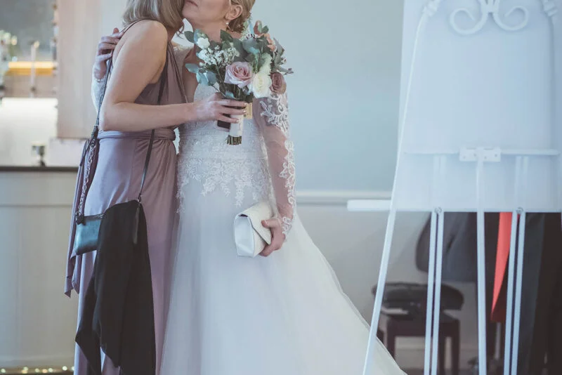 A bride kisses her bridesmaid in front of an easel.