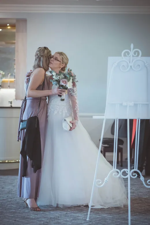 A bride kisses her bridesmaid in front of an easel.