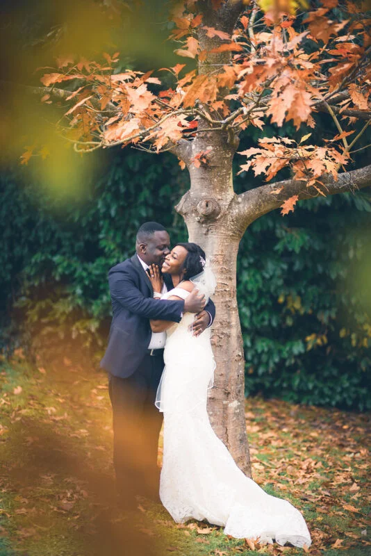 A bride and groom embracing under a tree in autumn.