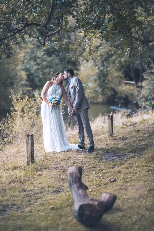 A bride and groom kissing in a wooded area.