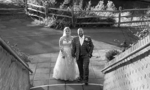 Black and white photo of a bride and groom walking down stairs.