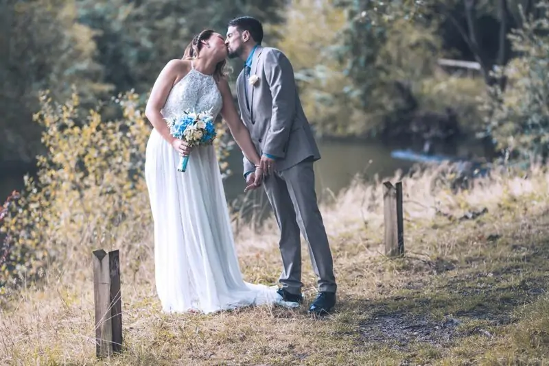 A bride and groom kissing in a wooded area.