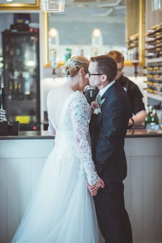 A bride and groom kissing in front of a bar.