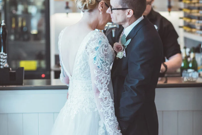 A bride and groom kissing in front of a bar.