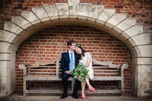 A bride and groom sitting on a bench in a brick archway.