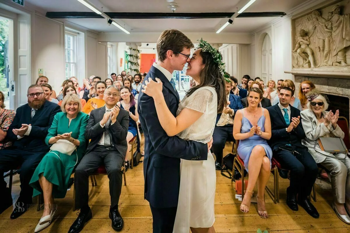 A bride and groom share a kiss in front of an audience.