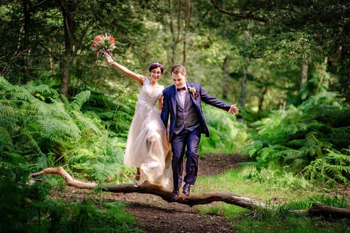 A bride and groom standing on a branch in the woods.