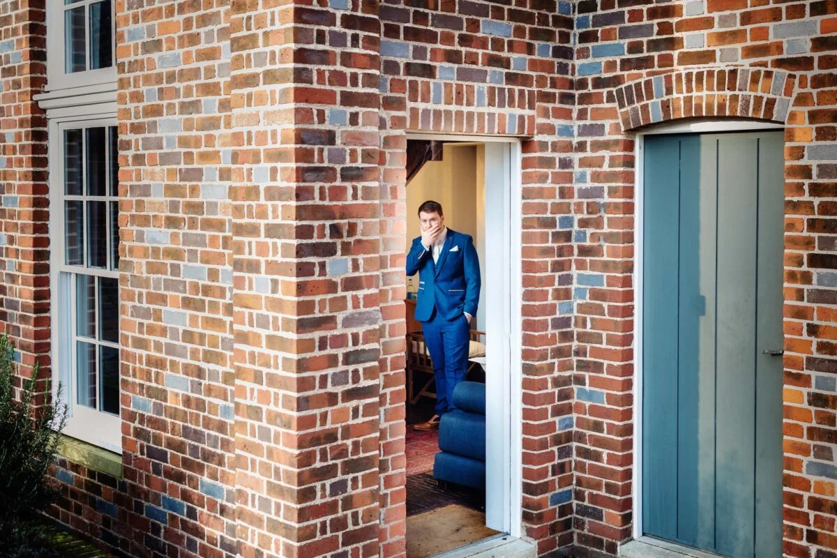 A man in a suit standing in the doorway of a brick house.