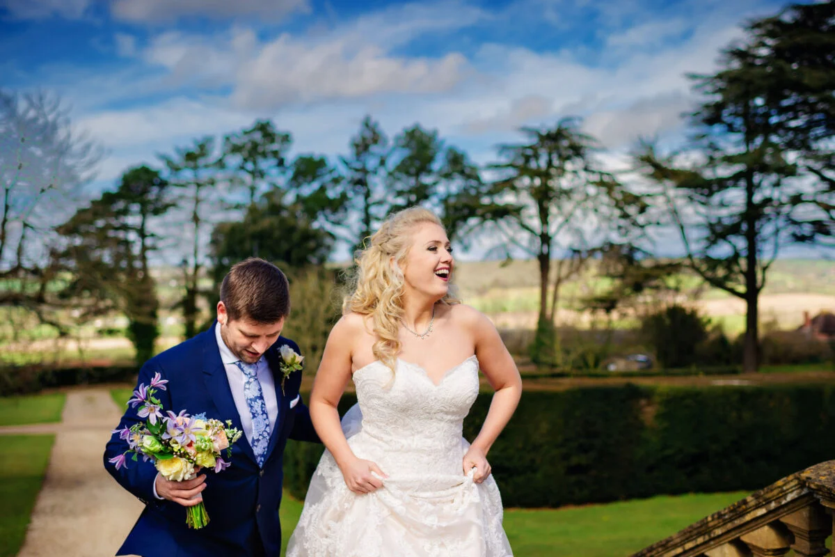 A bride and groom laughing on the steps of a country house.