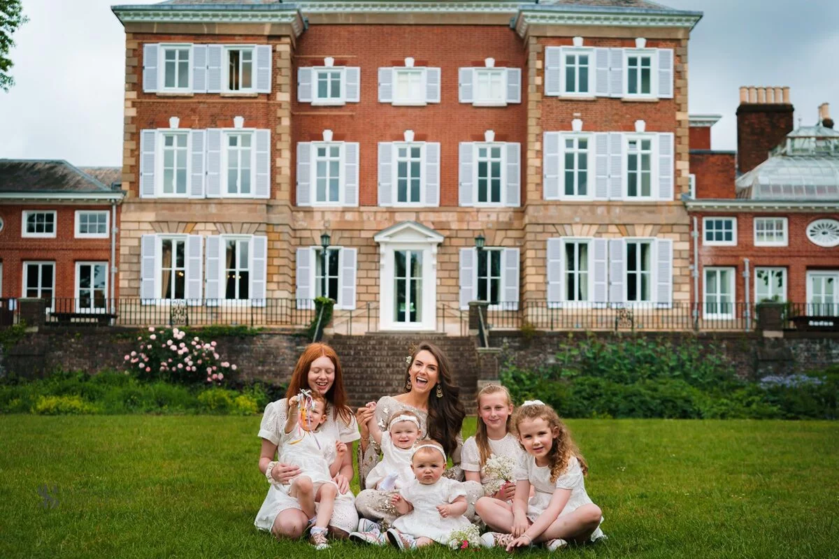 A family sits on the grass in front of a large mansion.