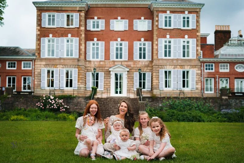 A family sits on the grass in front of a large mansion.