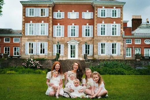 A family sits on the grass in front of a large mansion.