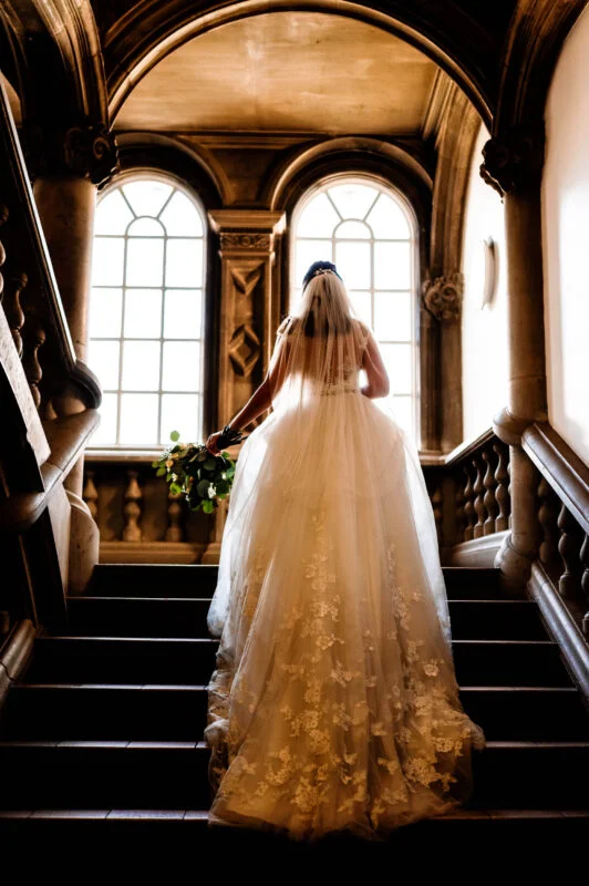 A bride is walking down the stairs in her wedding dress.