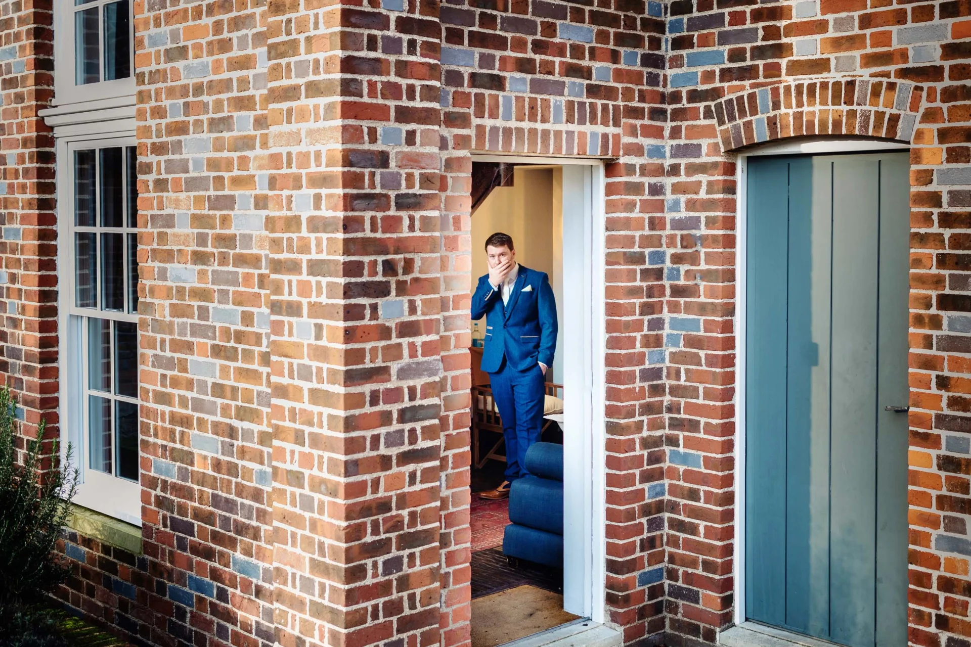 A man in a suit standing in the doorway of a brick house, cheap wedding. (listing)