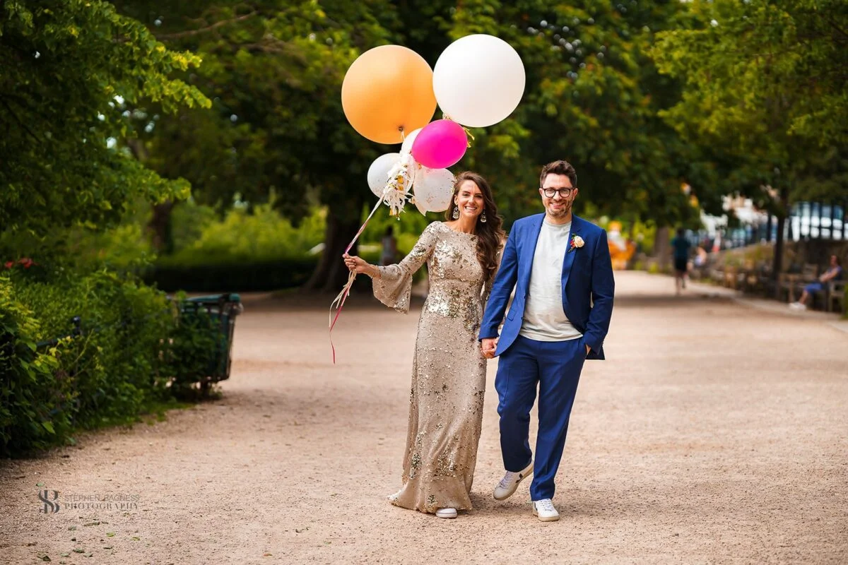 A bride and groom holding balloons in a park.