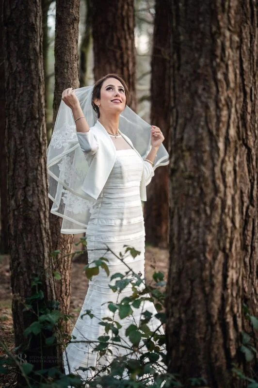 A bride in a wedding dress standing in the woods.