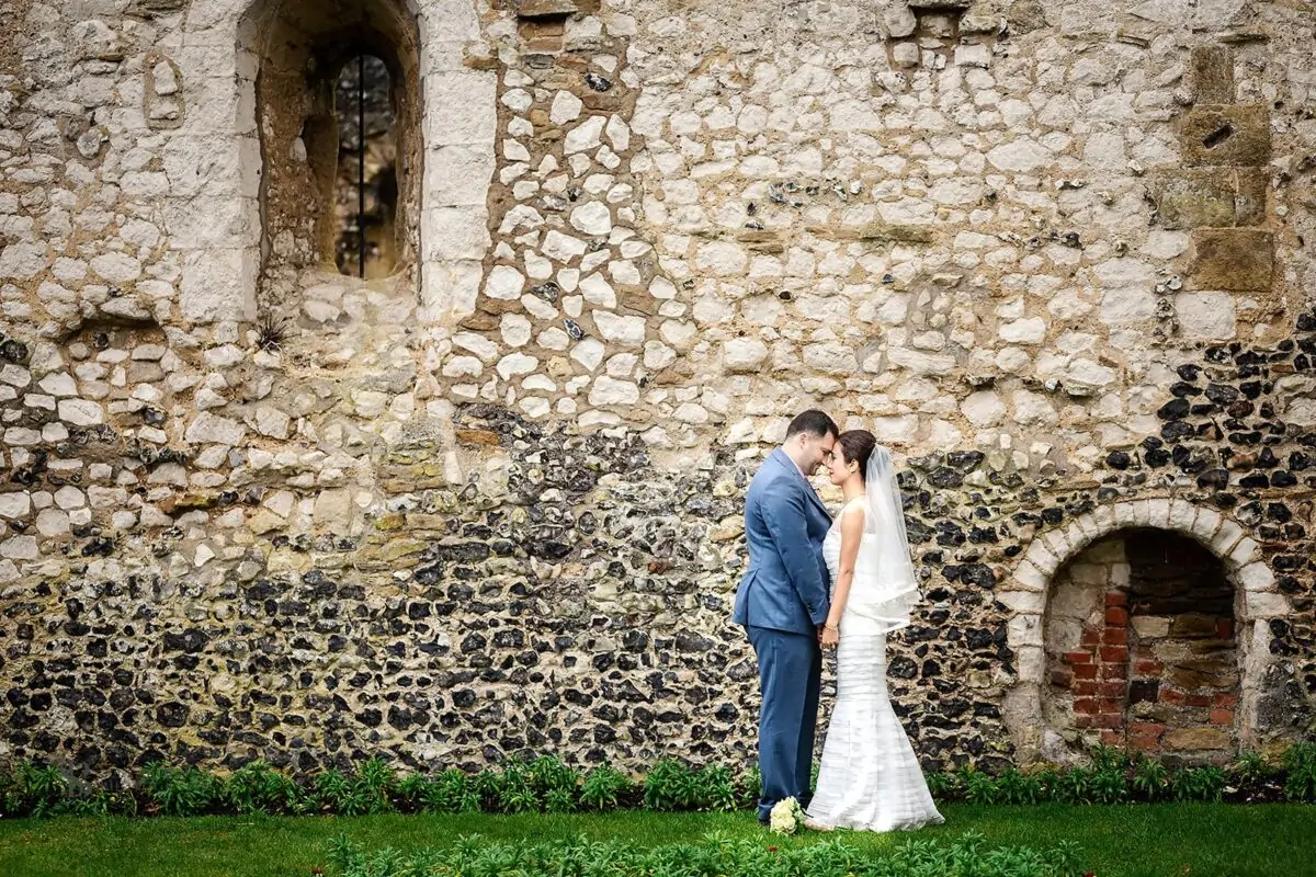 A bride and groom standing in front of a stone wall.