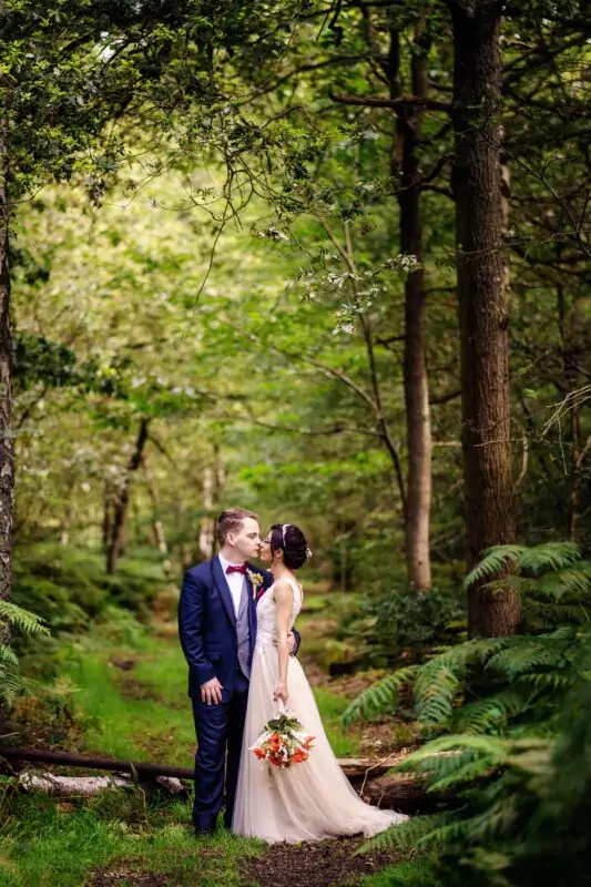 A bride and groom kissing in the woods.