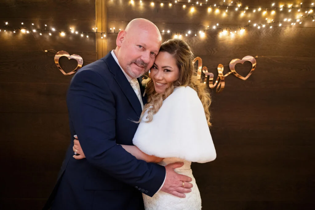 A bride and groom hugging in front of a string of lights.
