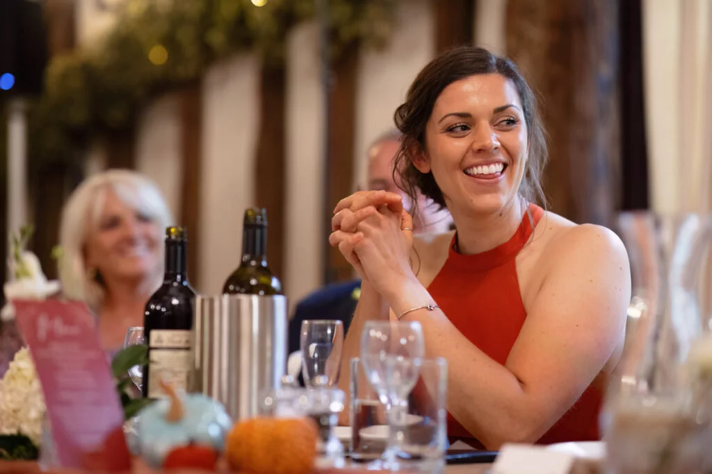 A woman smiles while sitting at a table at a wedding.