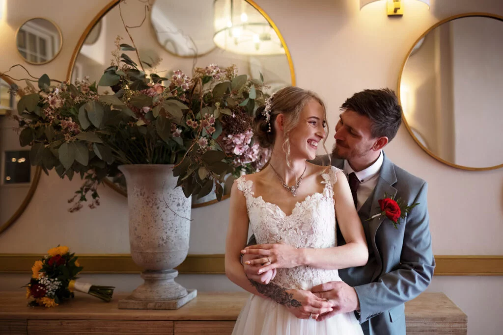 A bride and groom embracing in front of a mirror.
