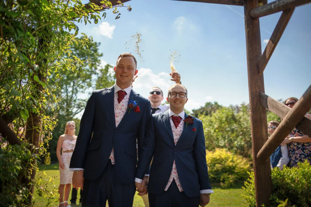 Two men in suits standing under a wooden archway.