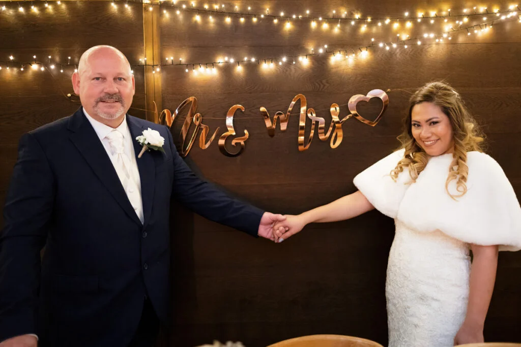 A bride and groom holding hands in front of a string of lights.