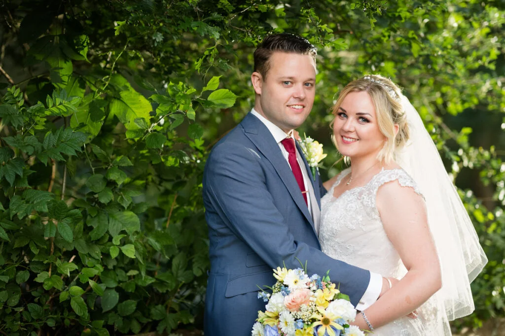 A bride and groom posing for a photo in a garden.