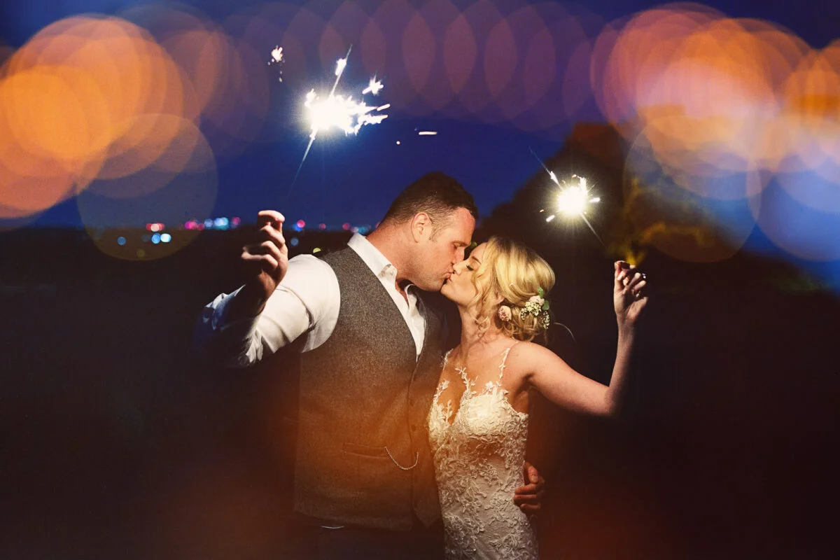 A bride and groom kissing while holding sparklers.